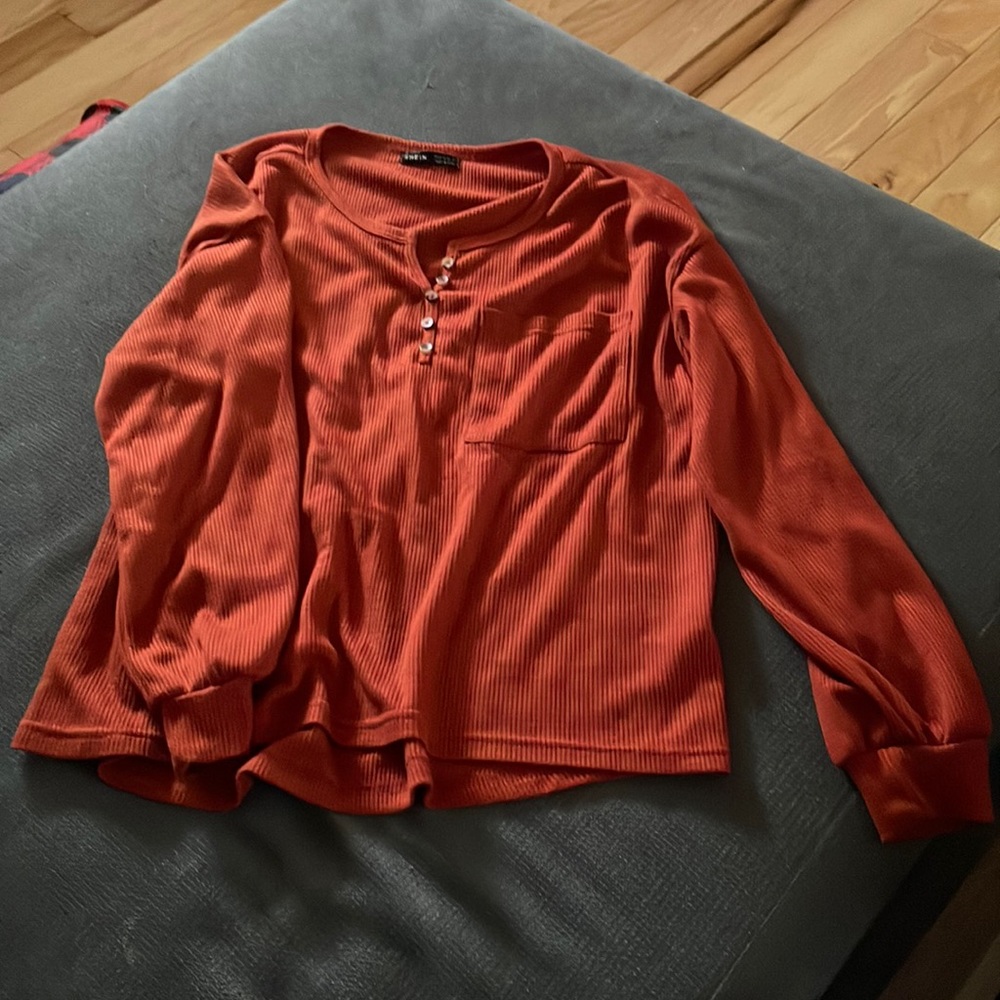 Burnt orange long sleeve top with buttons on the top and a small pocket